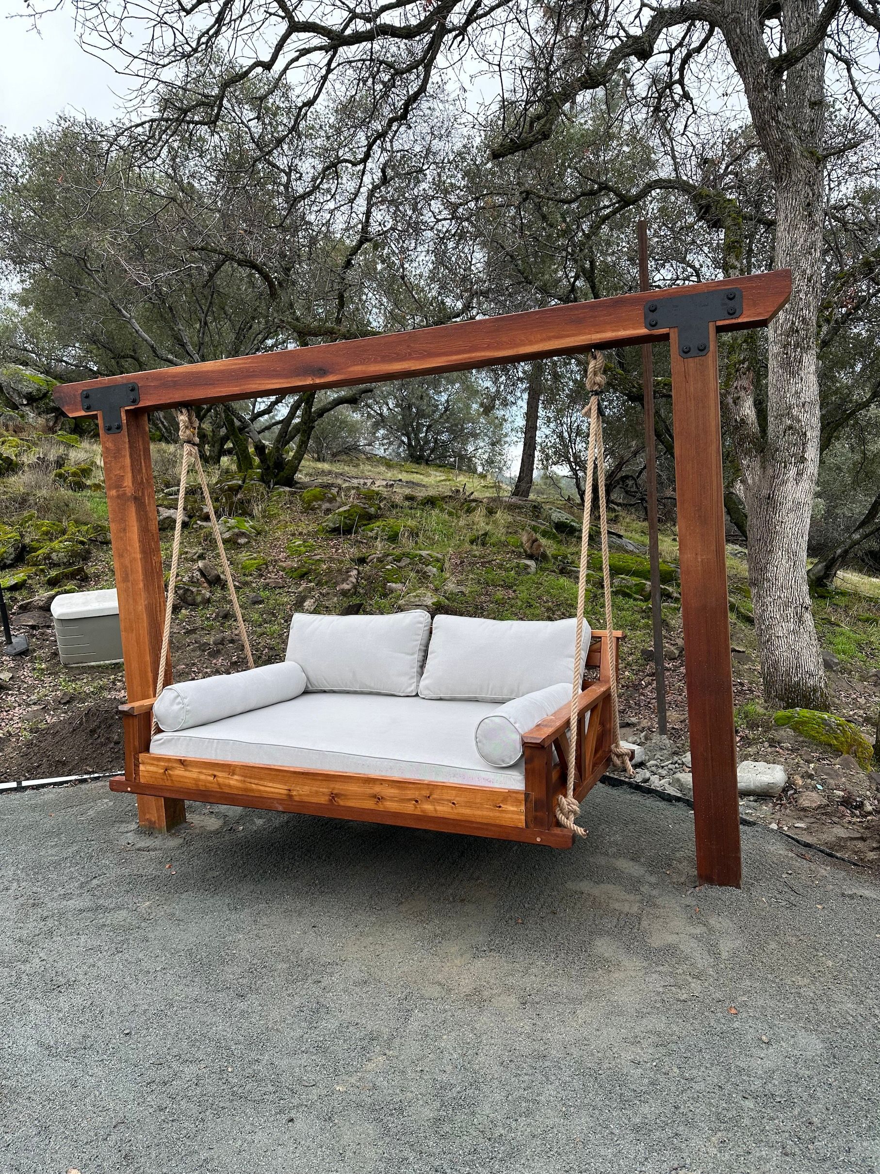 a wooden swing with white cushions is sitting on top of a gravel driveway .