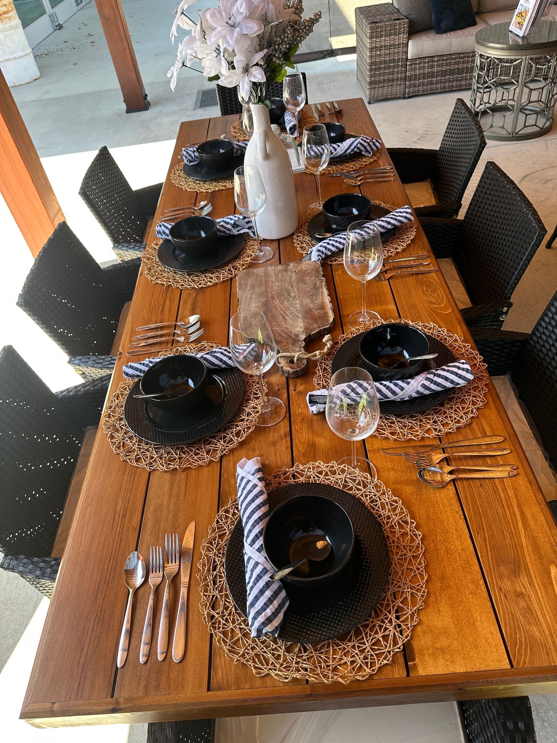 A wooden table with plates , bowls , utensils and a vase of flowers on it.