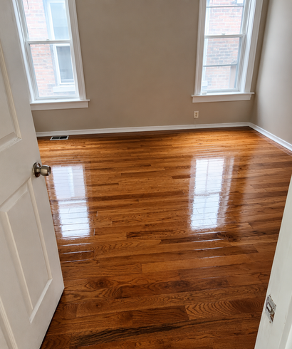 Empty room with glossy hardwood floors and two windows, viewed from an open doorway