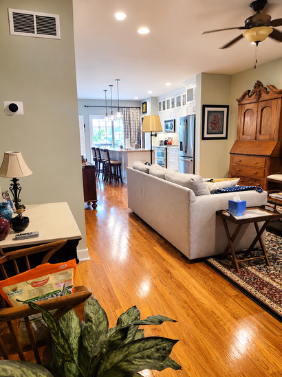 Bright living room with hardwood floors, beige sofa, ceiling fan, and wooden cabinet near a dining area