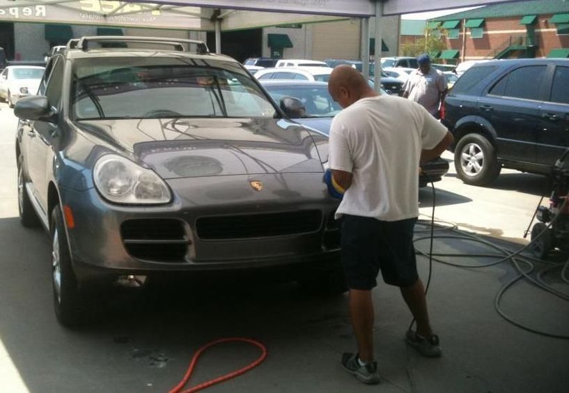 A man is polishing a porsche in a parking lot