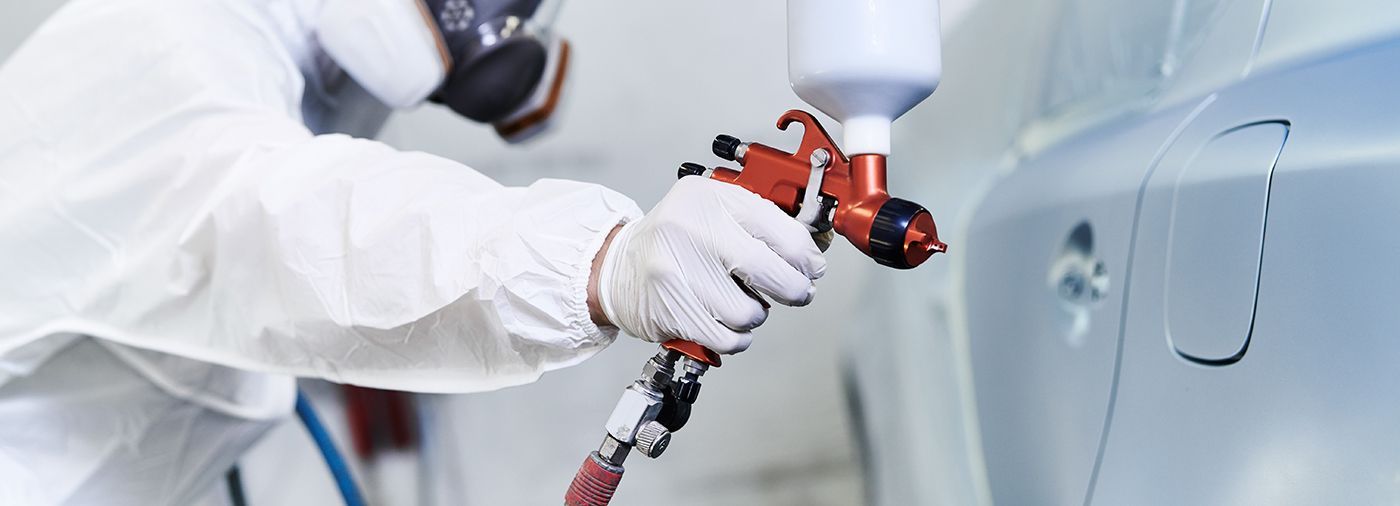 Worker spray-painting a silver car in a clean auto body shop