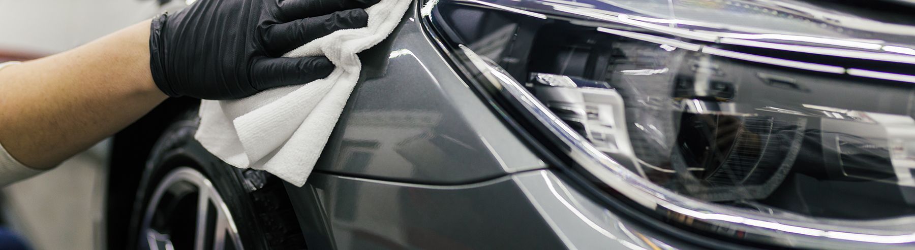Gloved hand polishing a silver car headlight and front fender