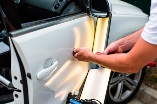 A man is repairing a car door with a tool.