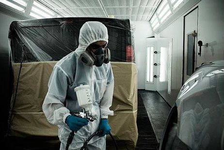 A man in a protective suit is painting a car in a paint booth.