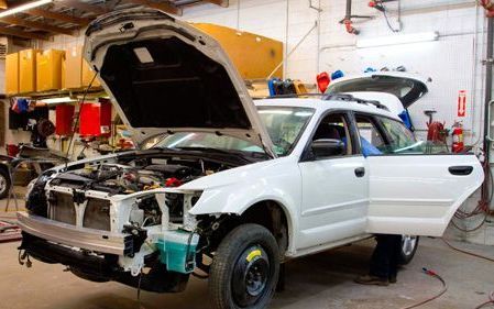 A white car with the hood open is being worked on in a garage.