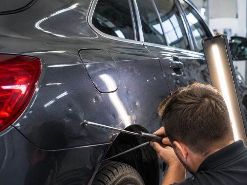 Mechanic inspecting a dark gray car door with a handheld tool in a repair shop