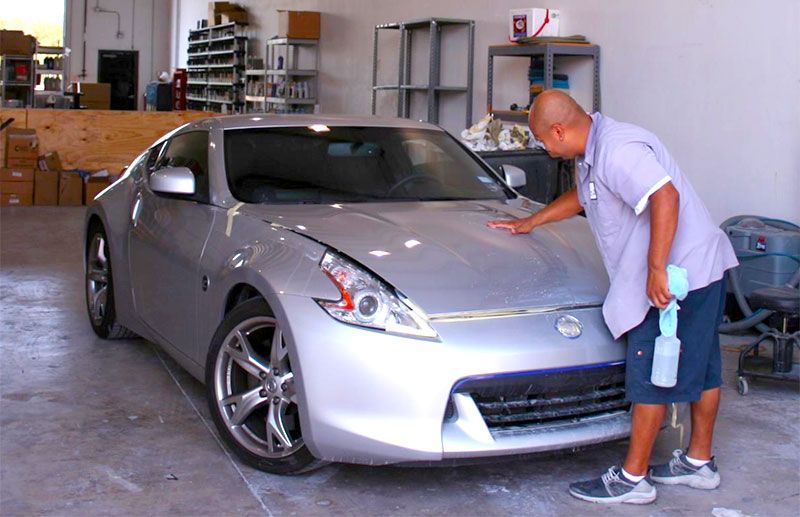 A man is cleaning a silver car in a garage