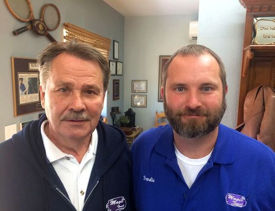 Two men in blue work shirts standing indoors, posing closely and looking at the camera.