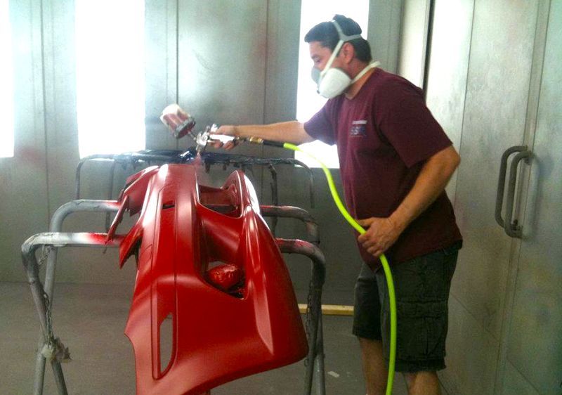 A man wearing a mask is spray painting a red bumper