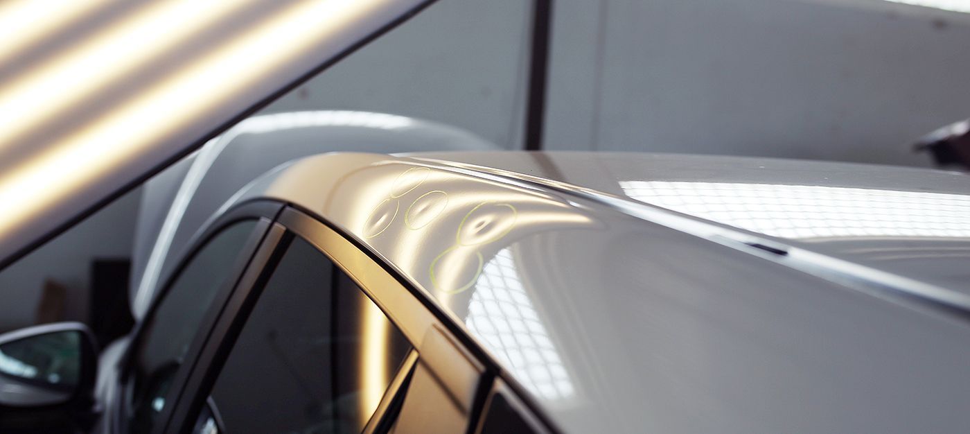 White car roof with multiple dents, likely for repair. Light shines on the surface.