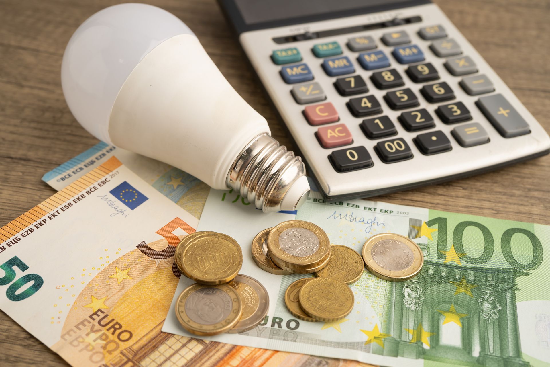 Light bulb, calculator, and euro banknotes and coins symbolizing energy costs and budgeting