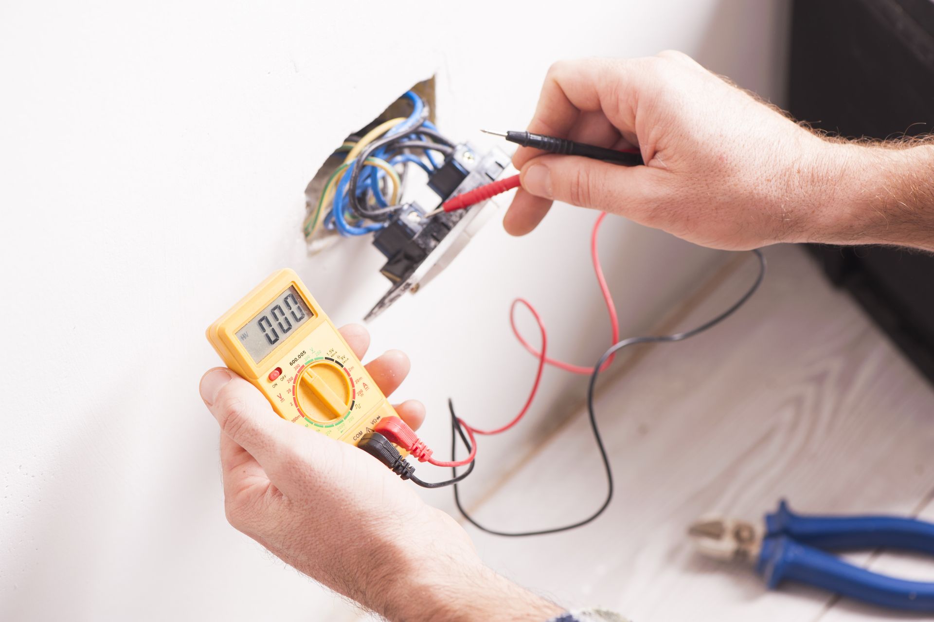 Hands using a multimeter to test wires in an electrical device on a white background