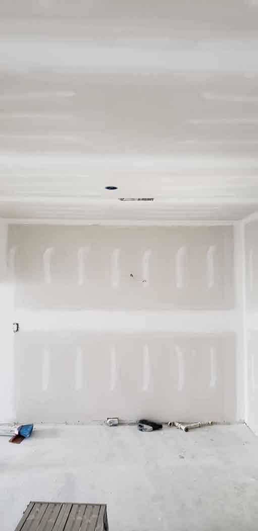 Interior of a room under construction with drywall on walls and ceiling. Tools are on the floor.