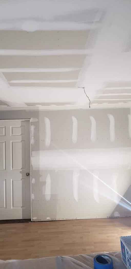 Room with unfinished drywall, a door, and wood flooring. A crack is visible in the ceiling.