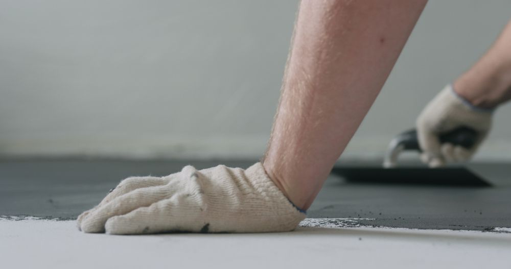 A Man Is Laying Concrete On The Floor With A Trowel — B & C Donnachie Concrete Contractors in Atherton, QLD
