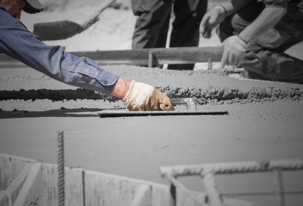 A Man Is Using A Trowel To Spread Concrete On A Construction Site — B & C Donnachie Concrete Contractors in Smithfield, QLD