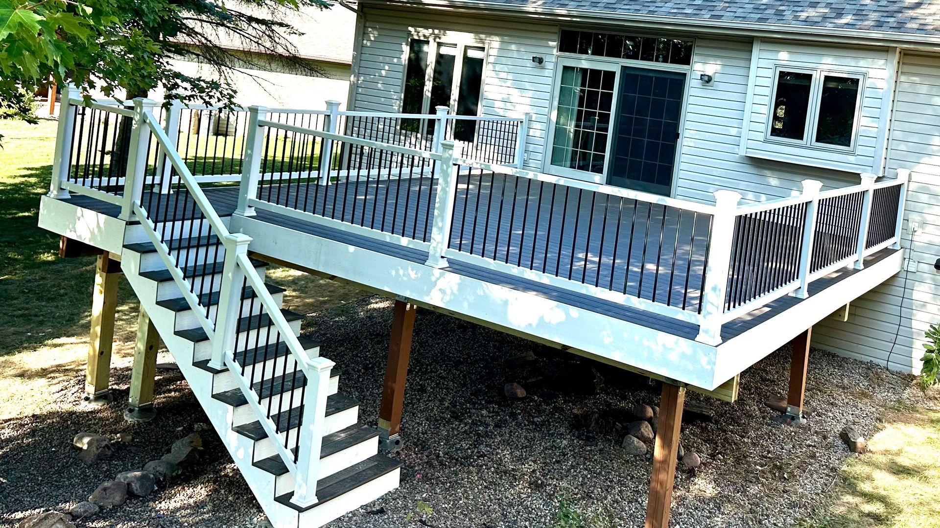 Elevated composite deck with white railings and dark gray decking on a tan ranch home