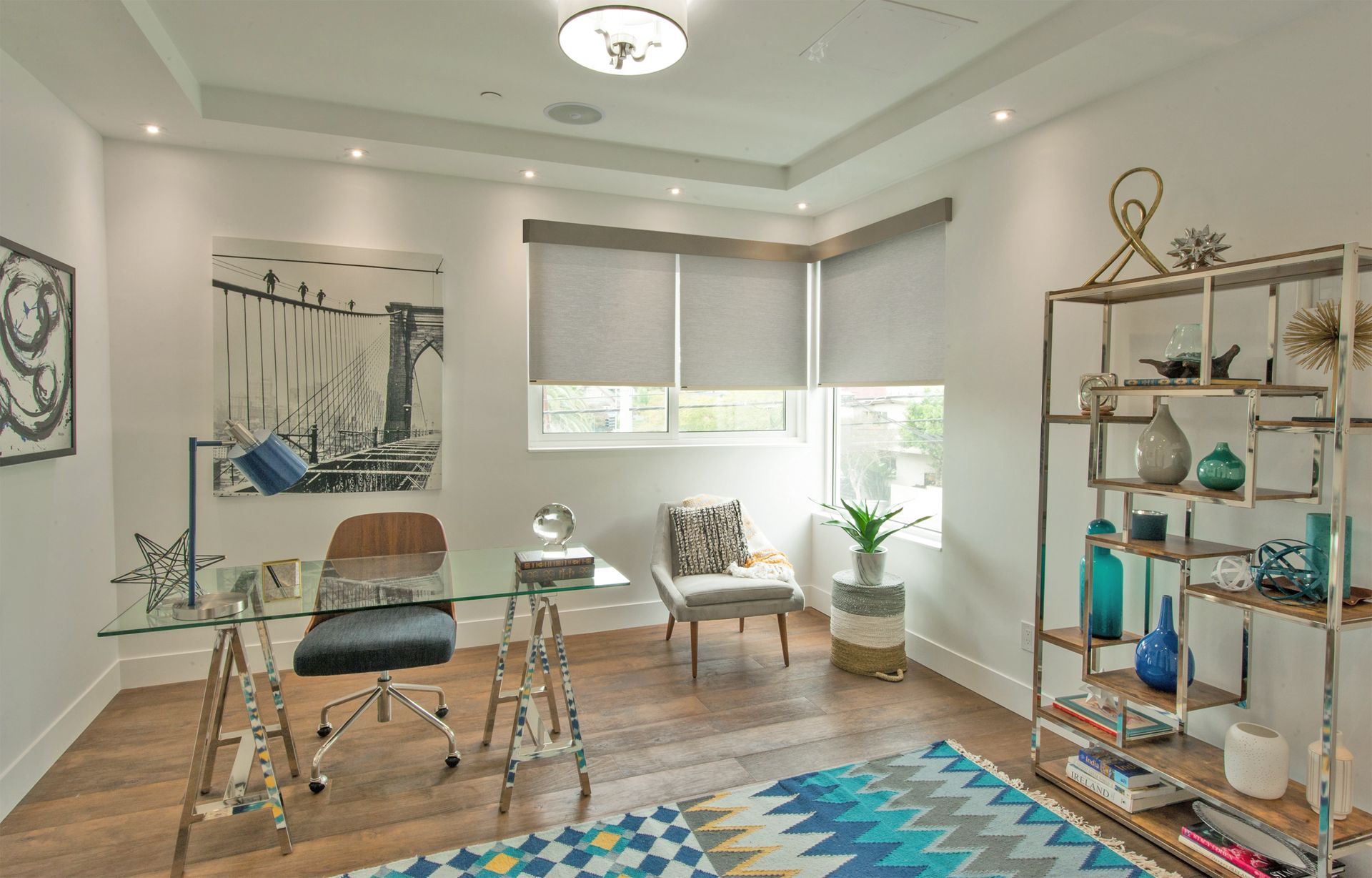 Home office with a glass desk, metal shelving, and colorful rug.