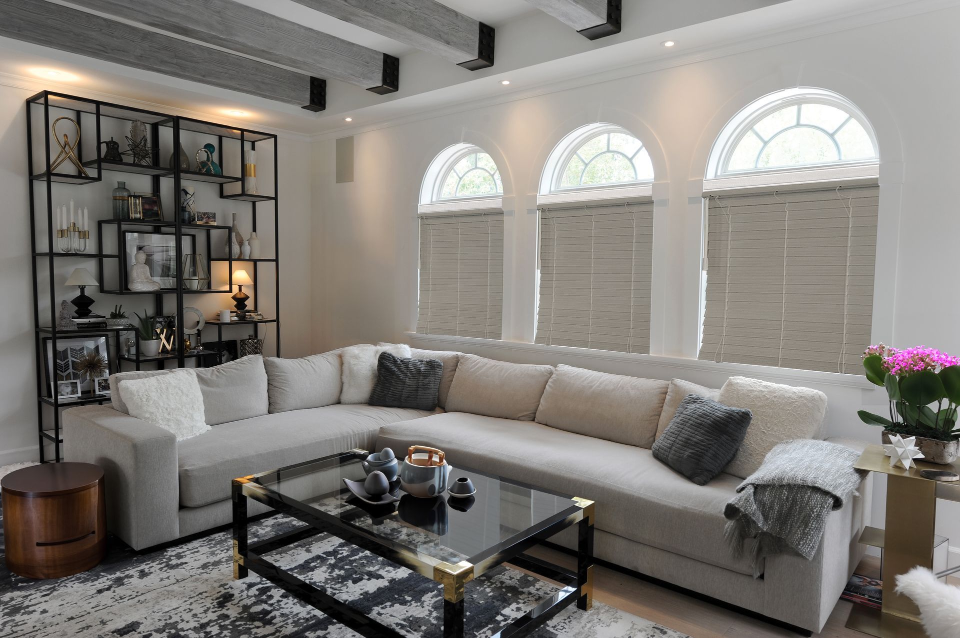 Living room with a large gray sectional sofa, arched windows, and a black and gold bookshelf.