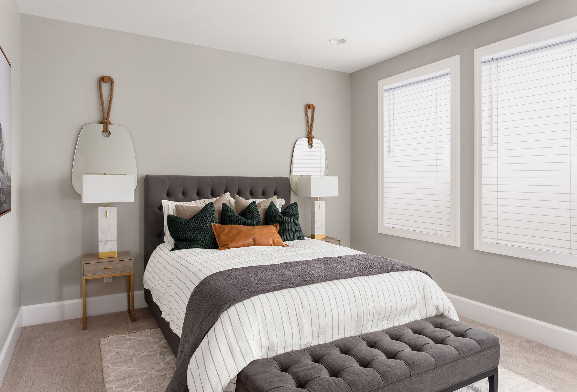 Bedroom with gray walls, bed with decorative pillows, two mirrors, and window.