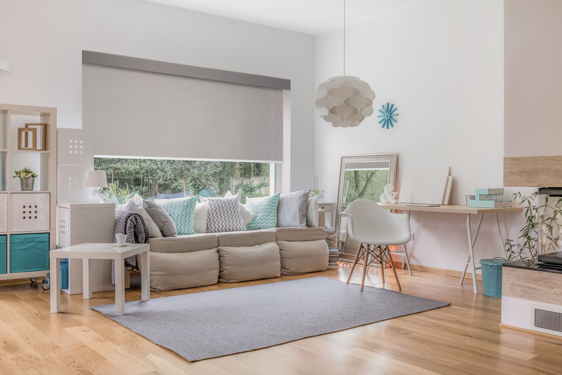 Bright living room with a neutral-toned sofa, large window with blinds, and wooden floors.