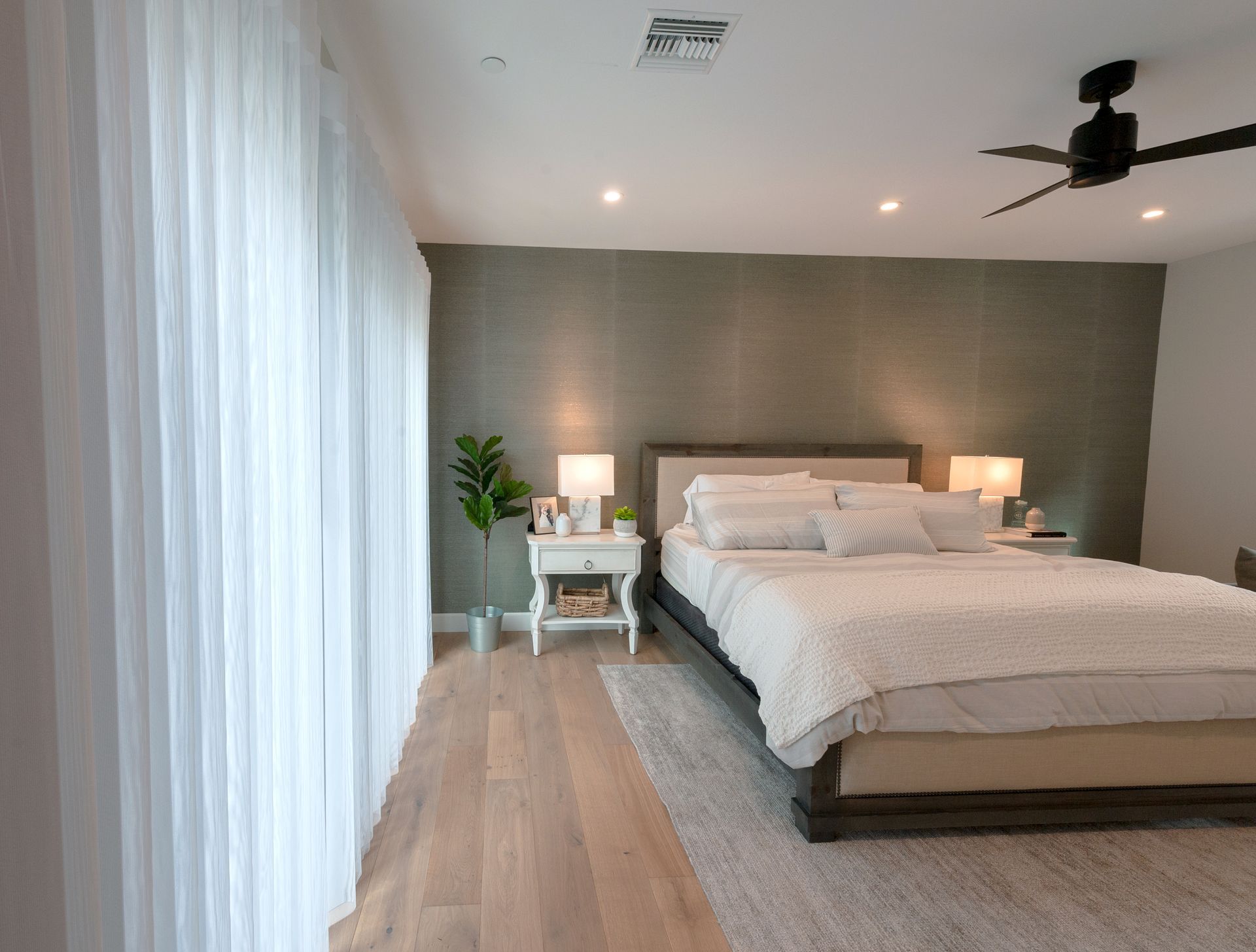 Bedroom with a bed, nightstands, sheer curtains, and a green accent wall.