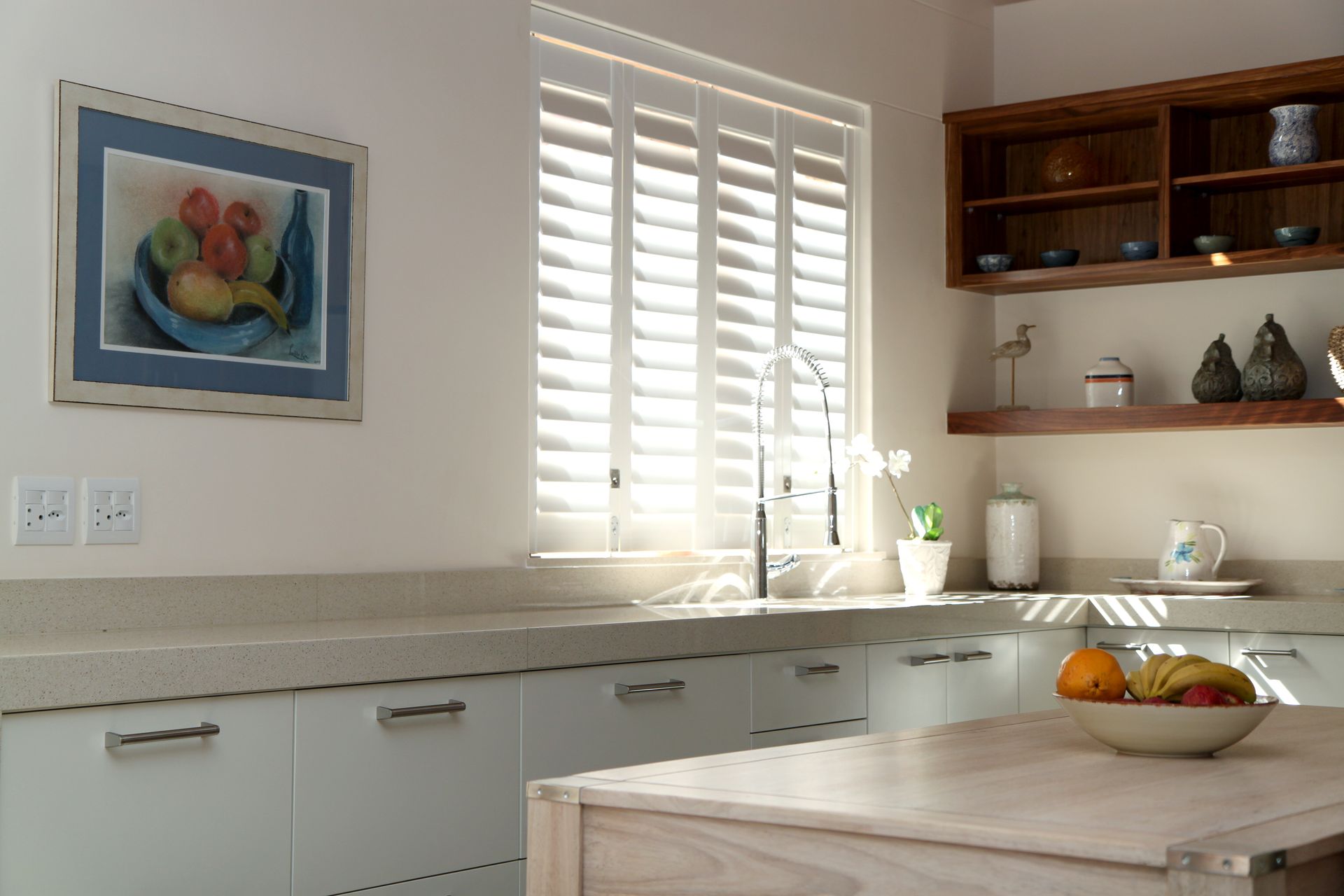 Kitchen with white cabinets, light wood island, window with blinds, and artwork.