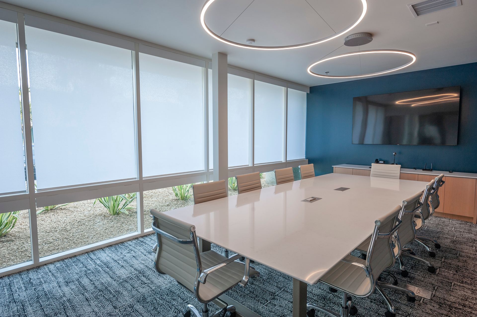 Conference room with a large white table, chairs, and a TV on a blue wall.