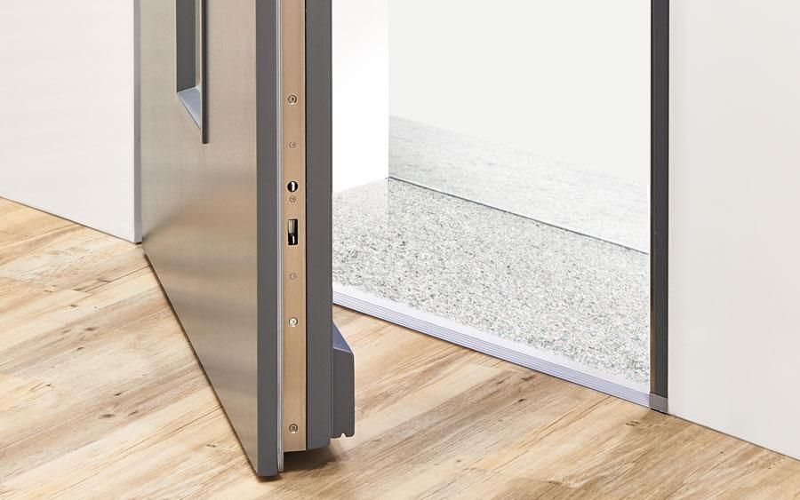 Partially open door with a silver bottom threshold and wood floor leading to a white room