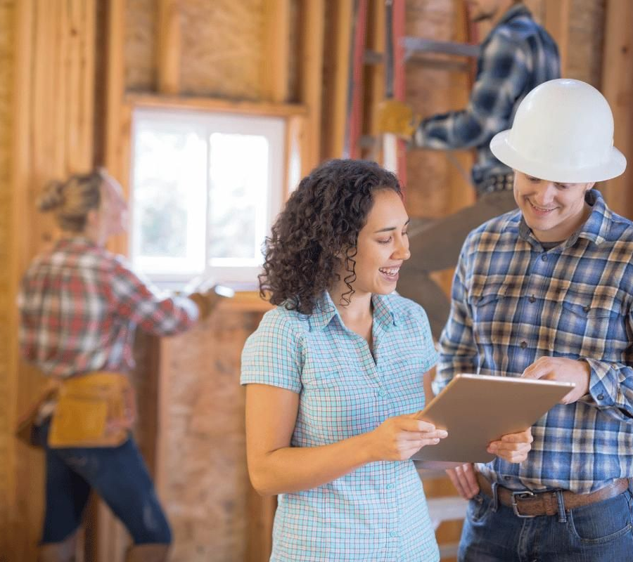 Two people review plans on a tablet inside a house under construction