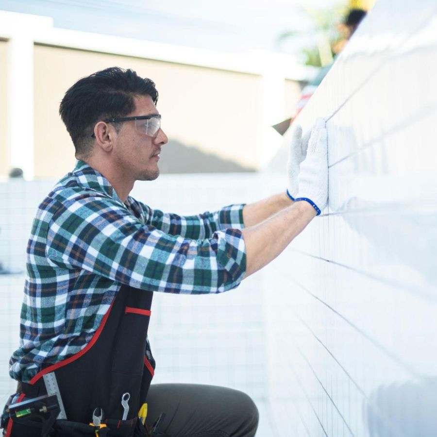 Worker in safety harness applying white tile or siding on an exterior wall