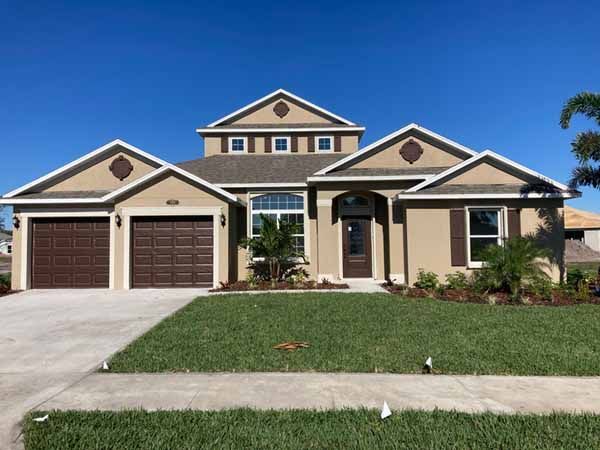 Two-story suburban house with a beige exterior, brown garage doors, and a green lawn under a blue sky