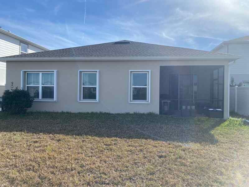 A single-story tan stucco home under a bright sky, featuring three front windows and a screened-in porch on the right side.