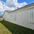 White house side wall with vertical metal panels and a grassy yard under a partly cloudy sky