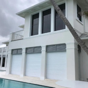 Modern white waterfront house with large windows, roll-down shutters, and a poolside palm tree