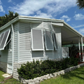 Light gray house with white shutters, stone trim, and a covered porch under a blue sky