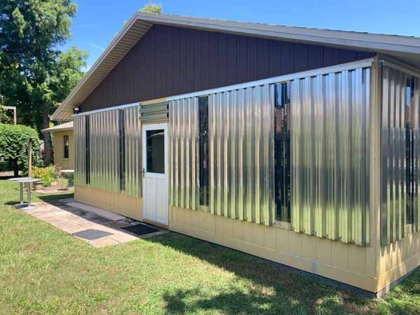 A long commercial or residential building structure with vertical corrugated metal sheets covering the entire glass facade on both sides of a central white entry door.