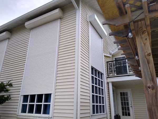 Corner of a house with two-story rolling shutters over windows.
