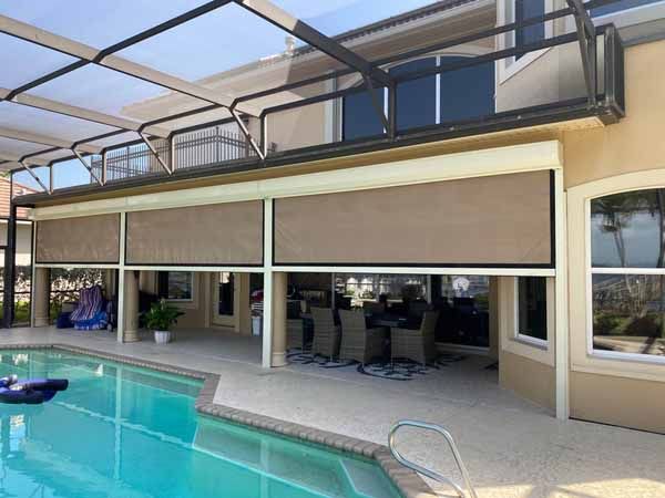 Enclosed pool deck with partially lowered sun shades over an outdoor dining set.