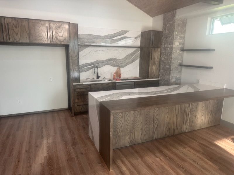 Modern kitchen with dark wood cabinetry, a waterfall island, and a marble-patterned backsplash.
