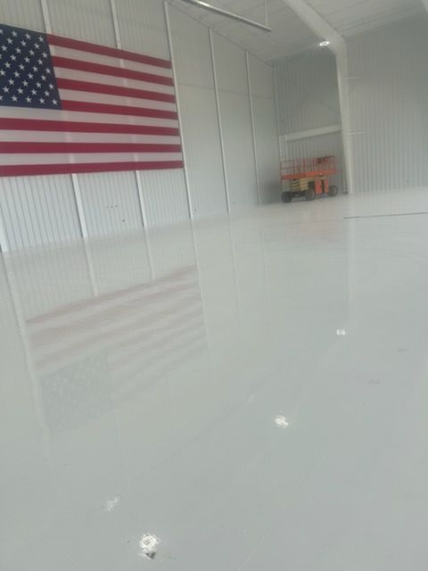 A large American flag mounted on a wall in a spacious warehouse with a highly reflective, glossy white concrete floor.
