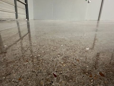 Polished, reflective concrete floor with visible aggregate stones in a room with white walls and a metal door frame.