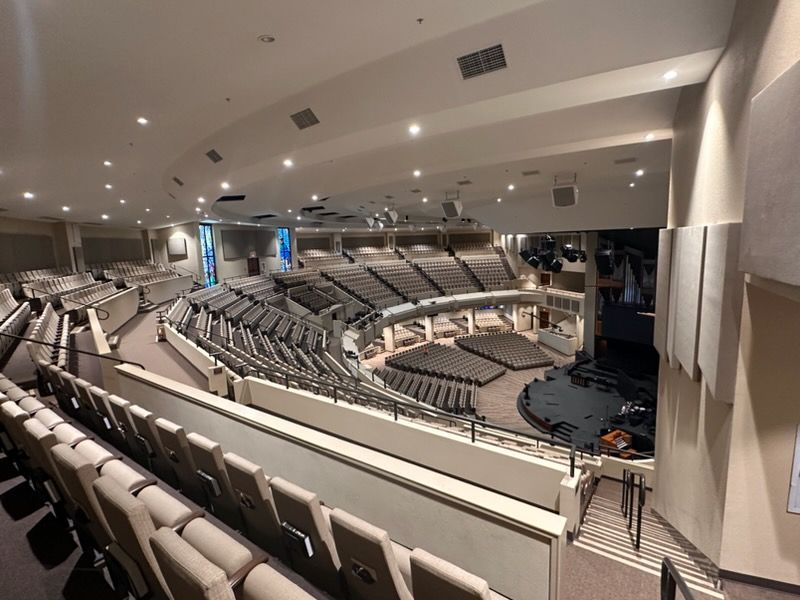 A high-angle view of a modern auditorium featuring curved rows of cushioned seats facing a central performance stage.