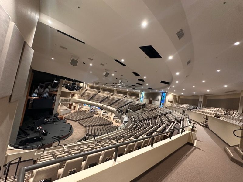 An elevated view of a large, empty auditorium with tiered rows of seats facing a stage under bright recessed lighting.