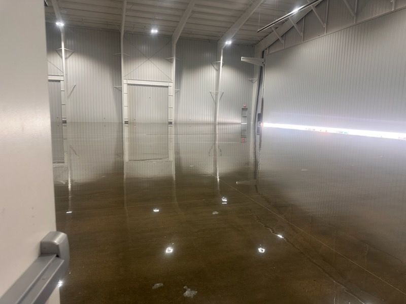 A large, empty industrial warehouse with polished concrete floors reflecting the ceiling lights and light-colored walls.