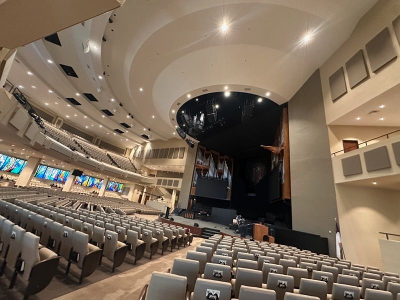 A large, modern, tiered auditorium with rows of gray seats facing an empty stage under dramatic lighting.
