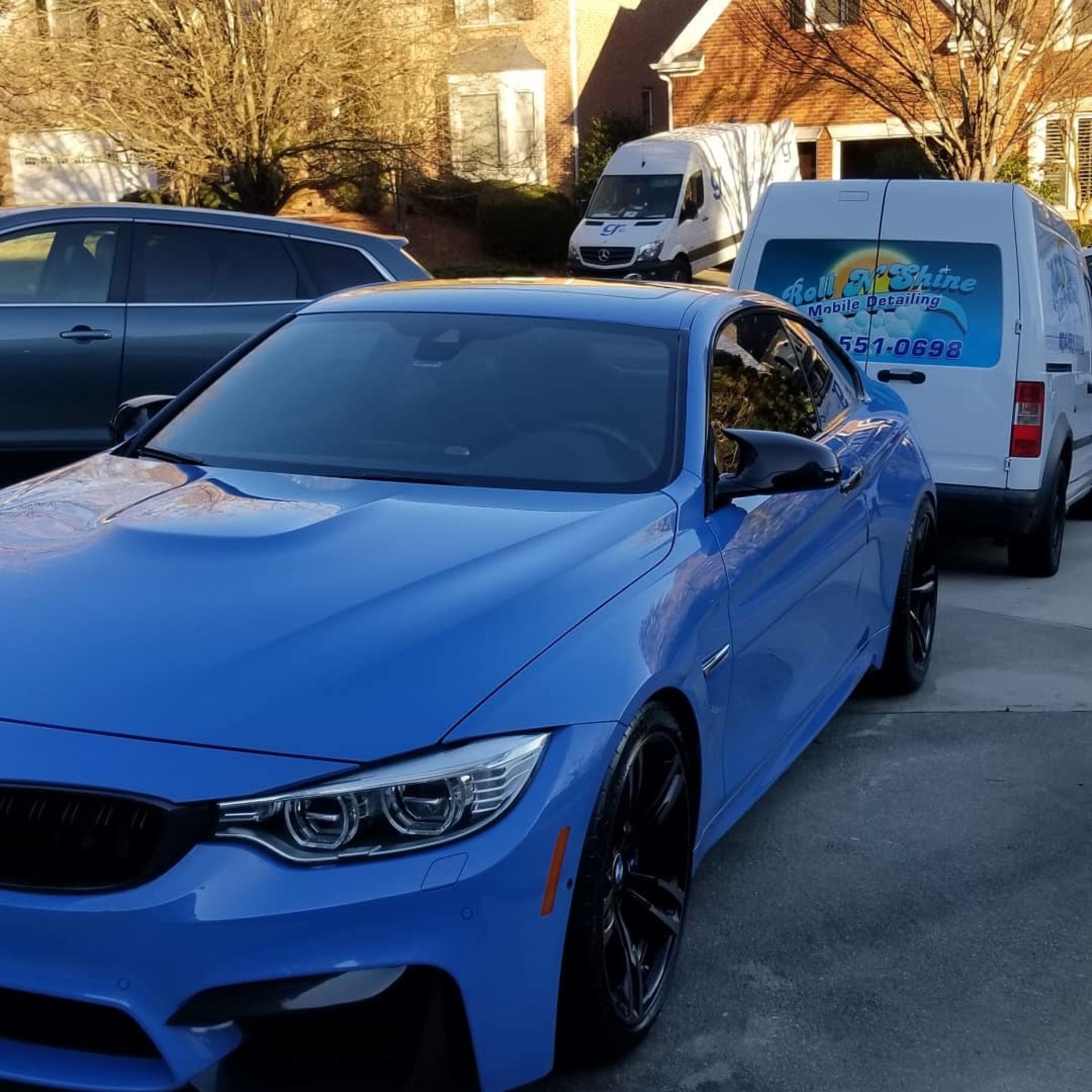 A blue car is parked next to a white van that says auto detailing