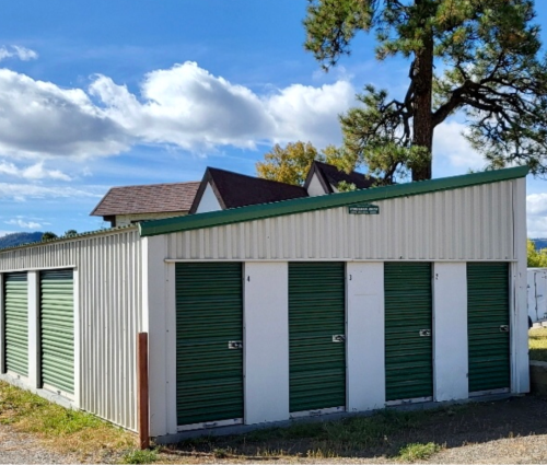 Storage units with green doors and white panels, under a blue sky.