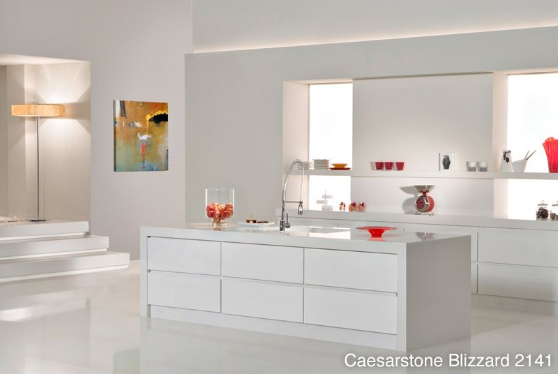 A kitchen with white cabinets and a large island that says caesarstone blizzard 2141